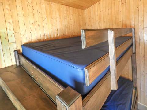A wooden bunk bed is installed in a room with wood-paneled walls.