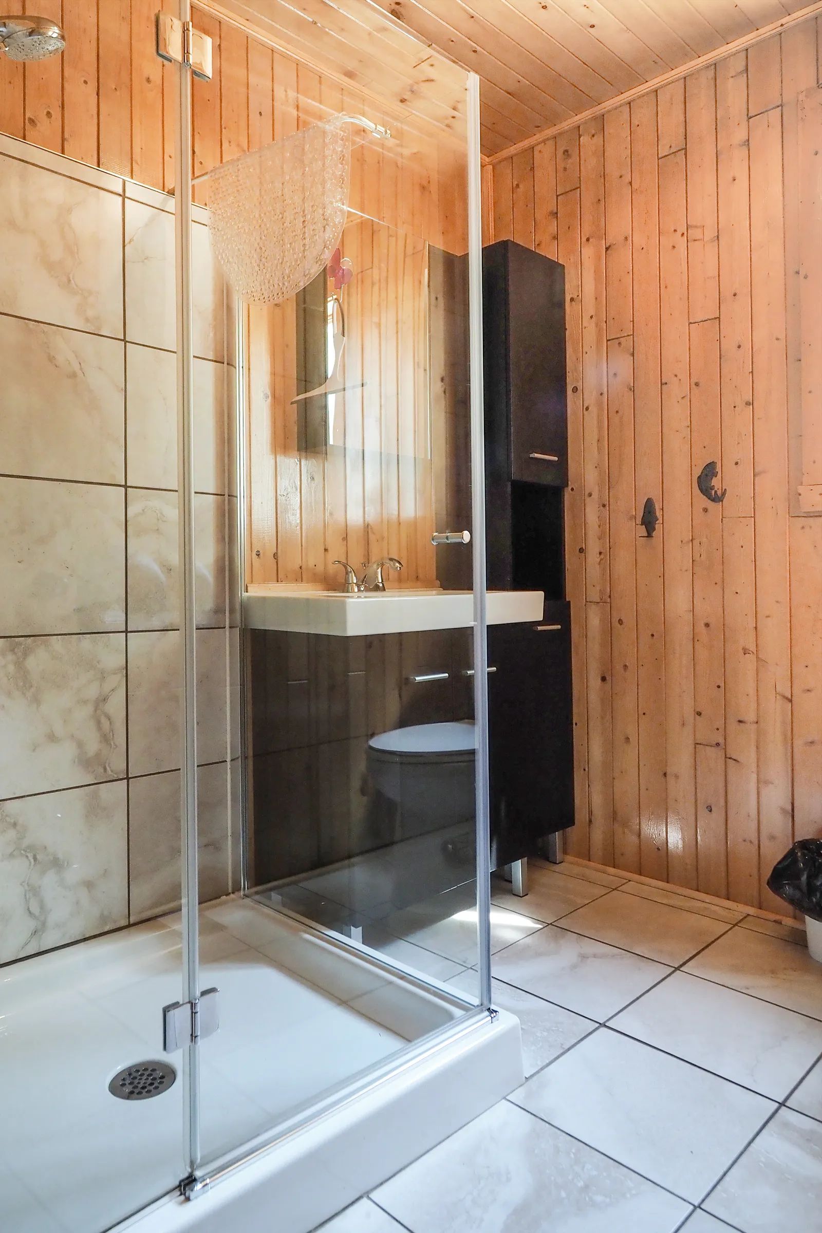View of the modern bathroom in cottage nine featuring a glass shower and wood paneling.