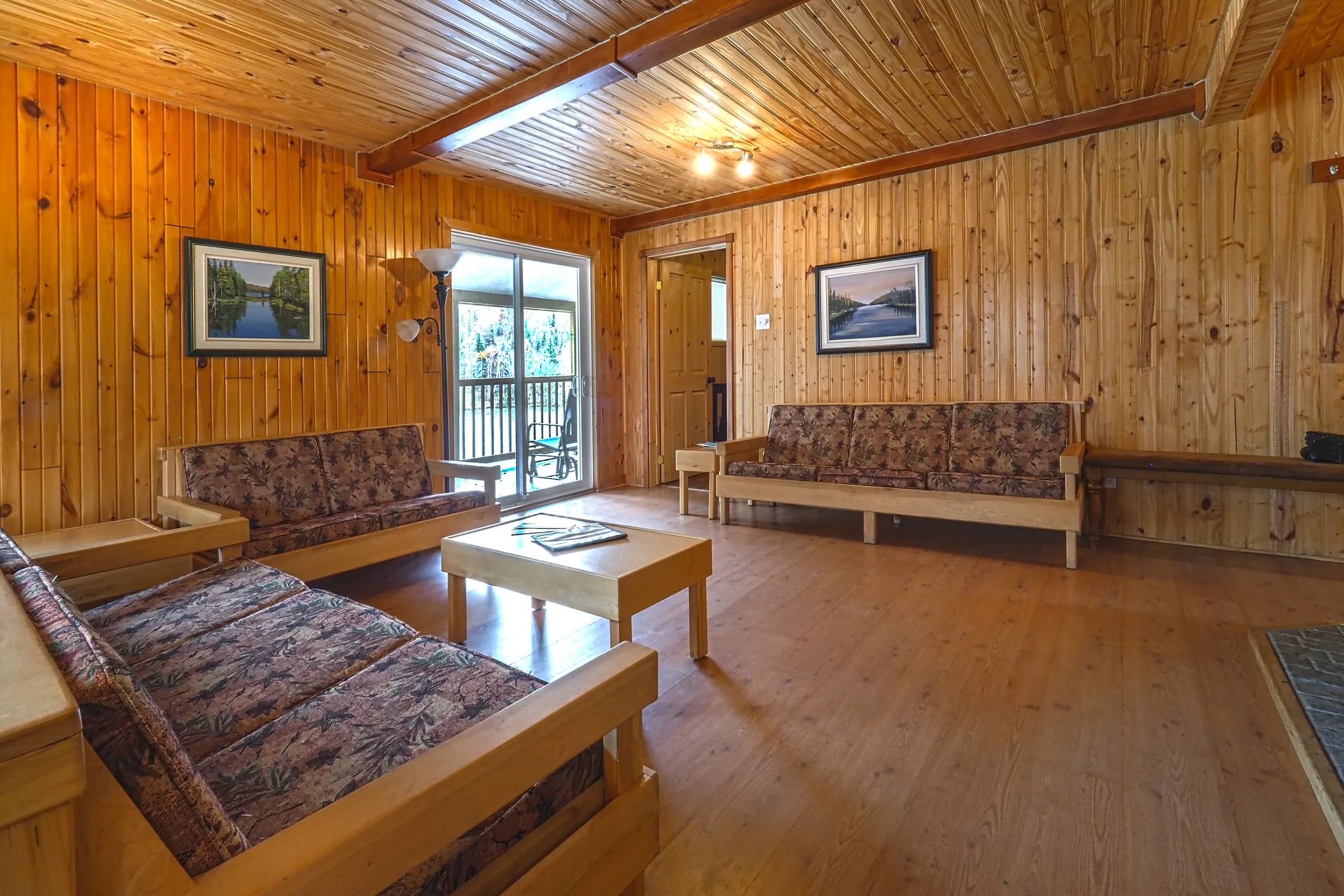 The cottage living room features wooden sofas and a patio door leading to a gallery.