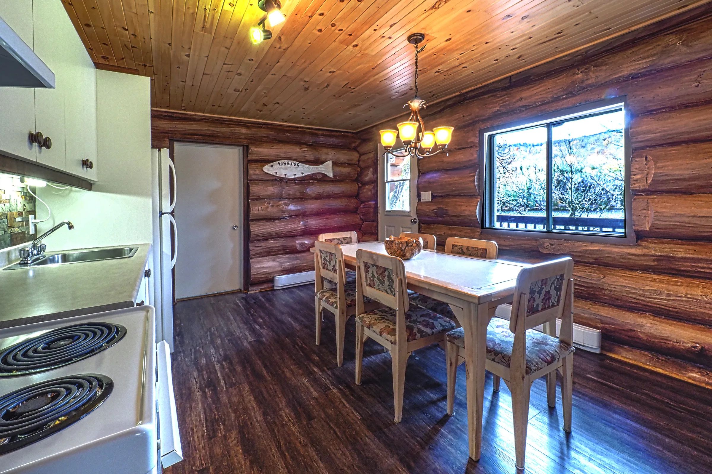 The dining area adjacent to the cabin's functional kitchen features log walls.