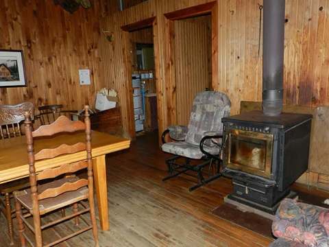 The cottage dining area features a wooden table and a wood-burning stove.