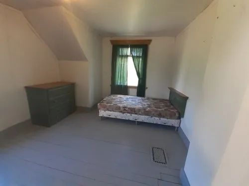 This simple bedroom features a bed and a dresser in the woodsman's house cabin.