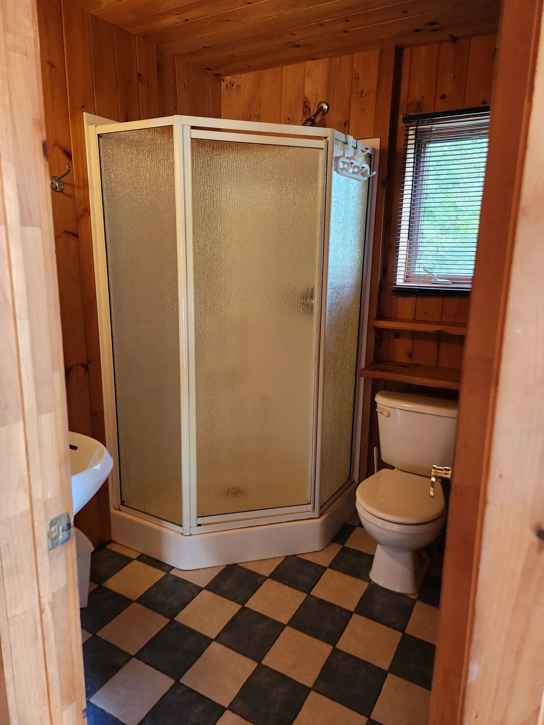 The cottage bathroom includes an enclosed shower and a toilet in a wood-paneled setting.