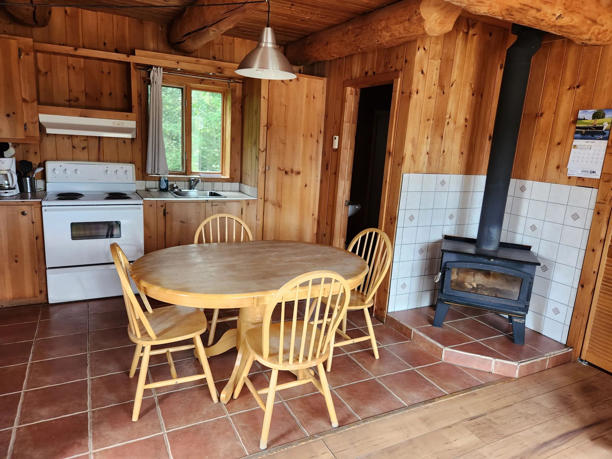 The dining area with wood stove and adjacent kitchen in this log cabin.