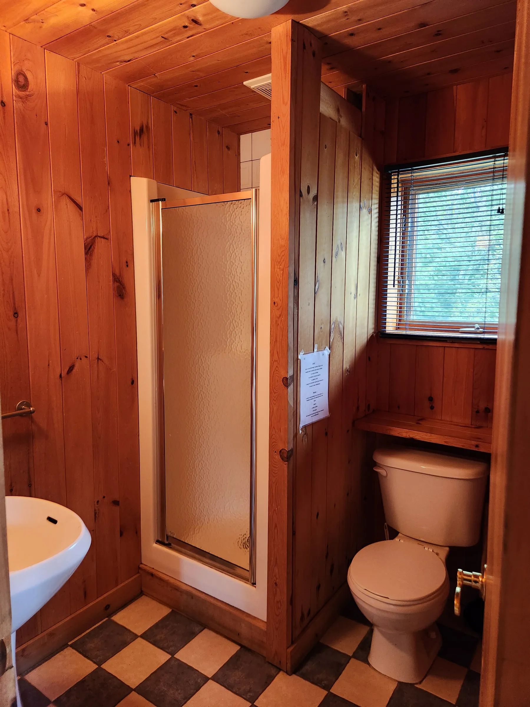 The cottage bathroom features a shower and a toilet with wood panelled walls.