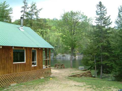 Cottage 17 features a porch overlooking a lake surrounded by forest with a picnic table.