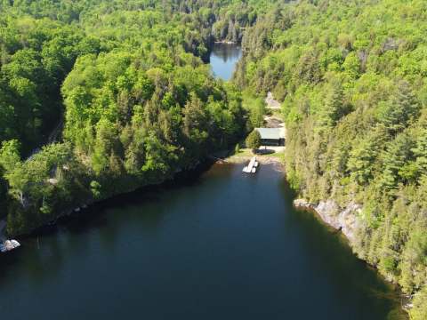 Aerial view of the cottage nestled by the lake in the middle of the forest.