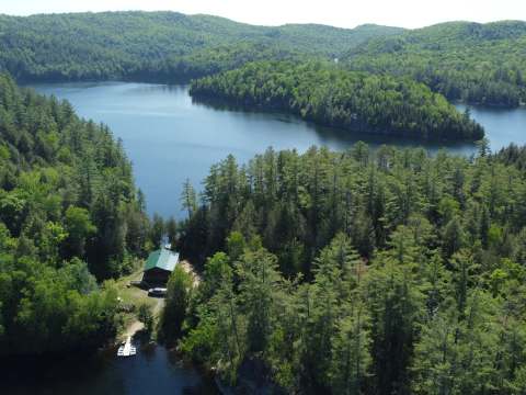 Aerial view of the cottage nestled by the lake in the middle of the forest.