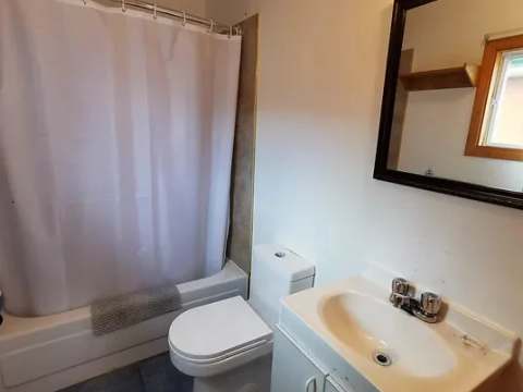 La salle de bain du chalet comprend une toilette, un lavabo et une baignoire avec douche.