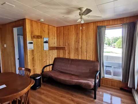 Coin salon avec divan-lit dans le chalet 14, incluant une table à manger et un ventilateur au plafond.