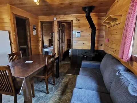 The interior of the cottage includes a dining table, a sofa, and a wood stove.