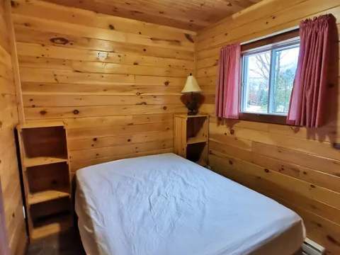 This rustic wooden bedroom features a double bed and a window with an outdoor view.