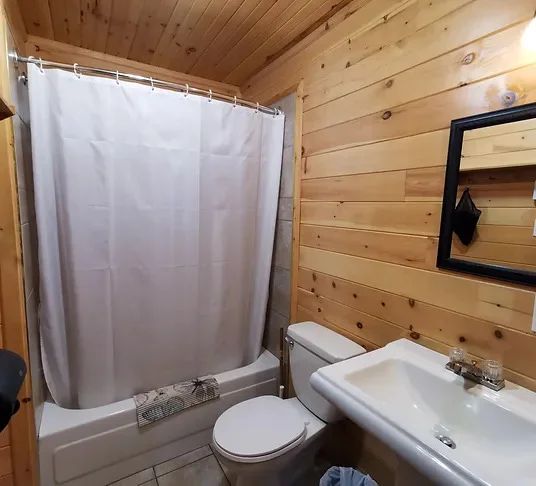 View of the cottage bathroom featuring natural wood walls and a bathtub with shower.