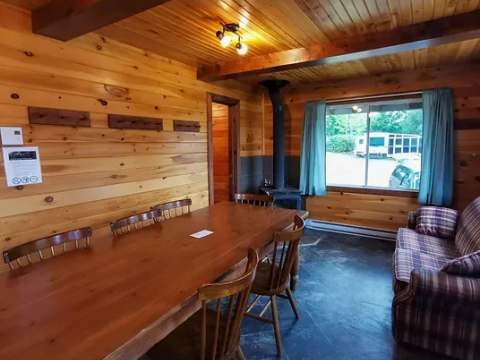 The cabin interior features a large wooden table and a living area with a wood stove.