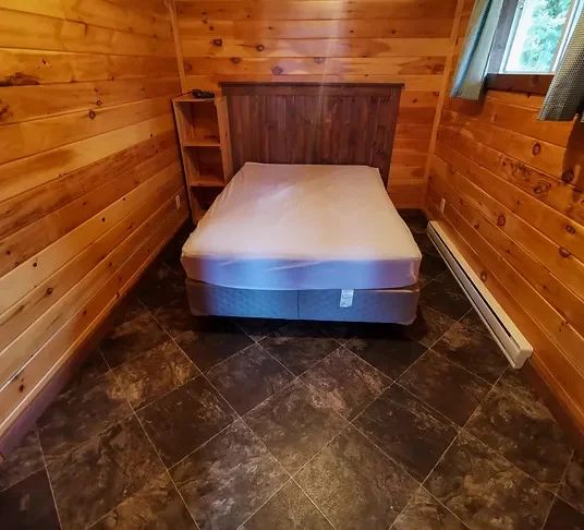 This cabin bedroom features a double bed with a wooden headboard and wood-paneled walls.