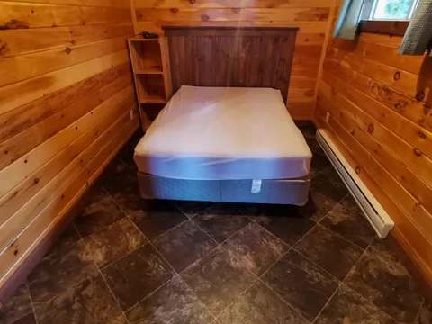 This cabin bedroom features a double bed with a wooden headboard and wood-paneled walls.