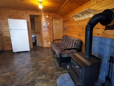 L'aire de vie du chalet comprend un poêle à bois, un sofa et un réfrigérateur.