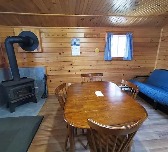 L'espace de vie du chalet comprend une table à manger et un poêle à bois.
