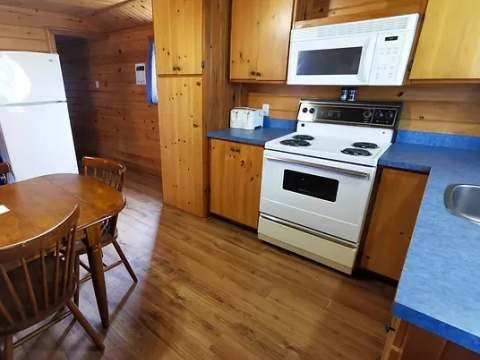 La cuisine fonctionnelle du chalet comprend une cuisinière, un réfrigérateur et une table à manger.