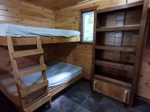 This rustic bedroom is equipped with wooden bunk beds and a storage shelf.