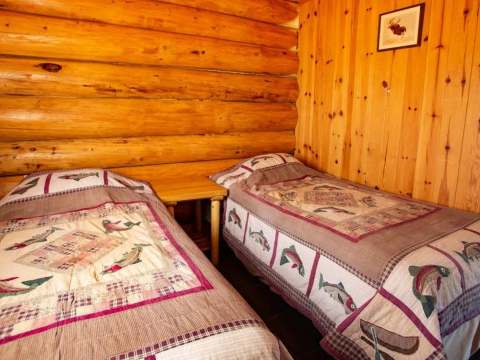 Two single beds with fish-themed quilts in a log cabin bedroom.