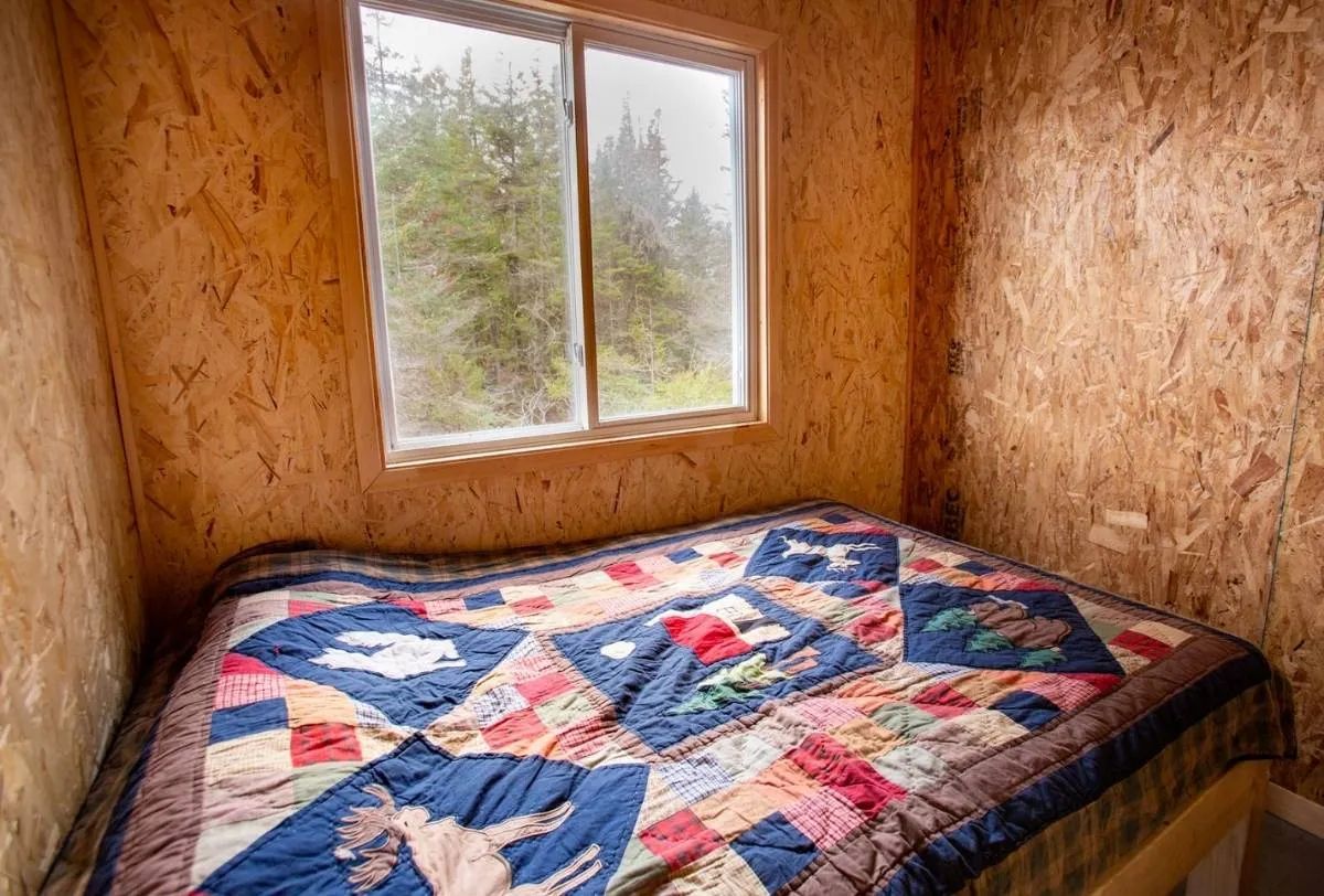 A bedroom with a quilt-covered bed and a view of the forest.