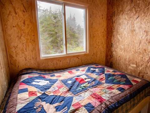 A bedroom with a quilt-covered bed and a view of the forest.