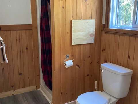 The bathroom in the Auger cottage includes a shower with a plaid curtain and a toilet.