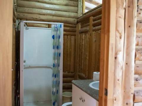La salle de bain du chalet comprend une douche et un lavabo encastré dans une structure en bois rond.