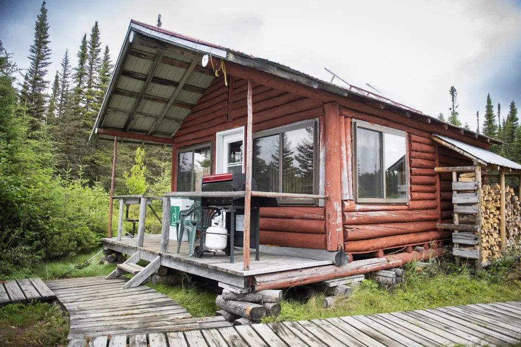 Le chalet numéro deux en bois rond possède une galerie avec un barbecue et une réserve de bois.