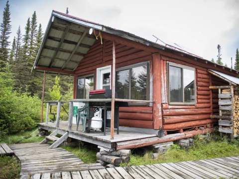 Le chalet numéro deux en bois rond possède une galerie avec un barbecue et une réserve de bois.