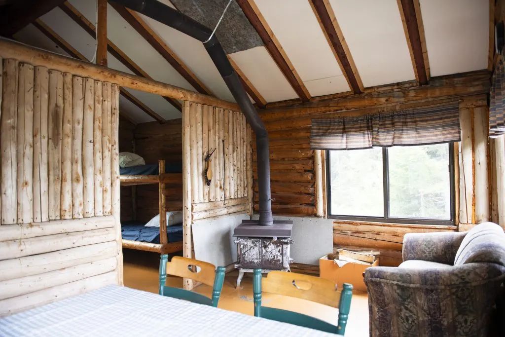 Vue de l'intérieur du chalet avec son coin salon, son poêle à bois et sa chambre à lits superposés.