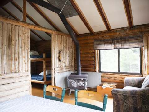 Vue de l'intérieur du chalet avec son coin salon, son poêle à bois et sa chambre à lits superposés.