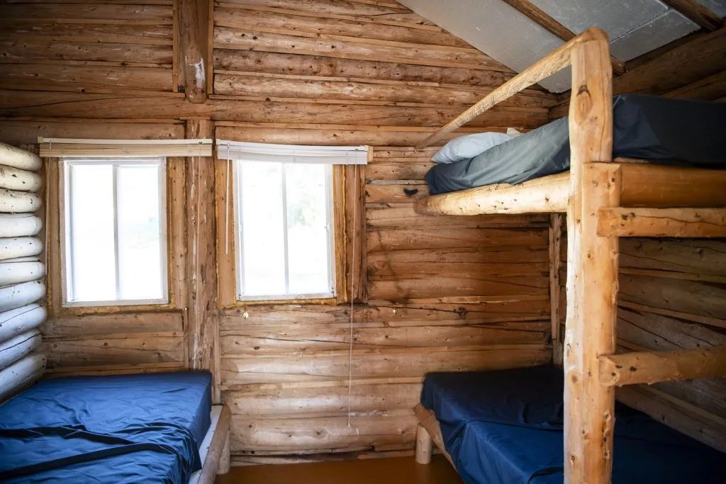 Cette chambre rustique est équipée de lits simples et de lits superposés en bois rond.