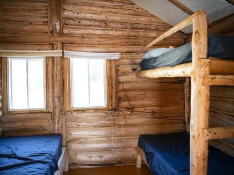 Cette chambre rustique est équipée de lits simples et de lits superposés en bois rond.