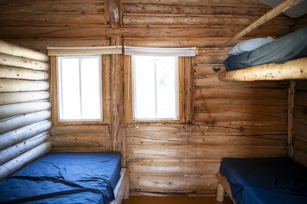 Vue de l'intérieur du chalet avec ses murs en bois rond et ses lits simples.