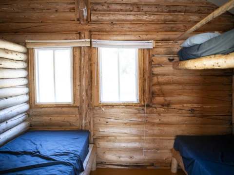 Vue de l'intérieur du chalet avec ses murs en bois rond et ses lits simples.