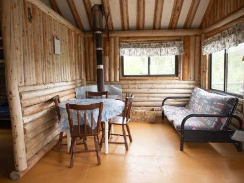 L'aire de vie du chalet comprend une table à manger et un canapé près du poêle à bois.