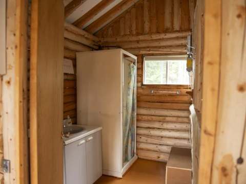 Vue de la salle de bain du chalet avec douche et lavabo intégrés dans une structure en bois rond.
