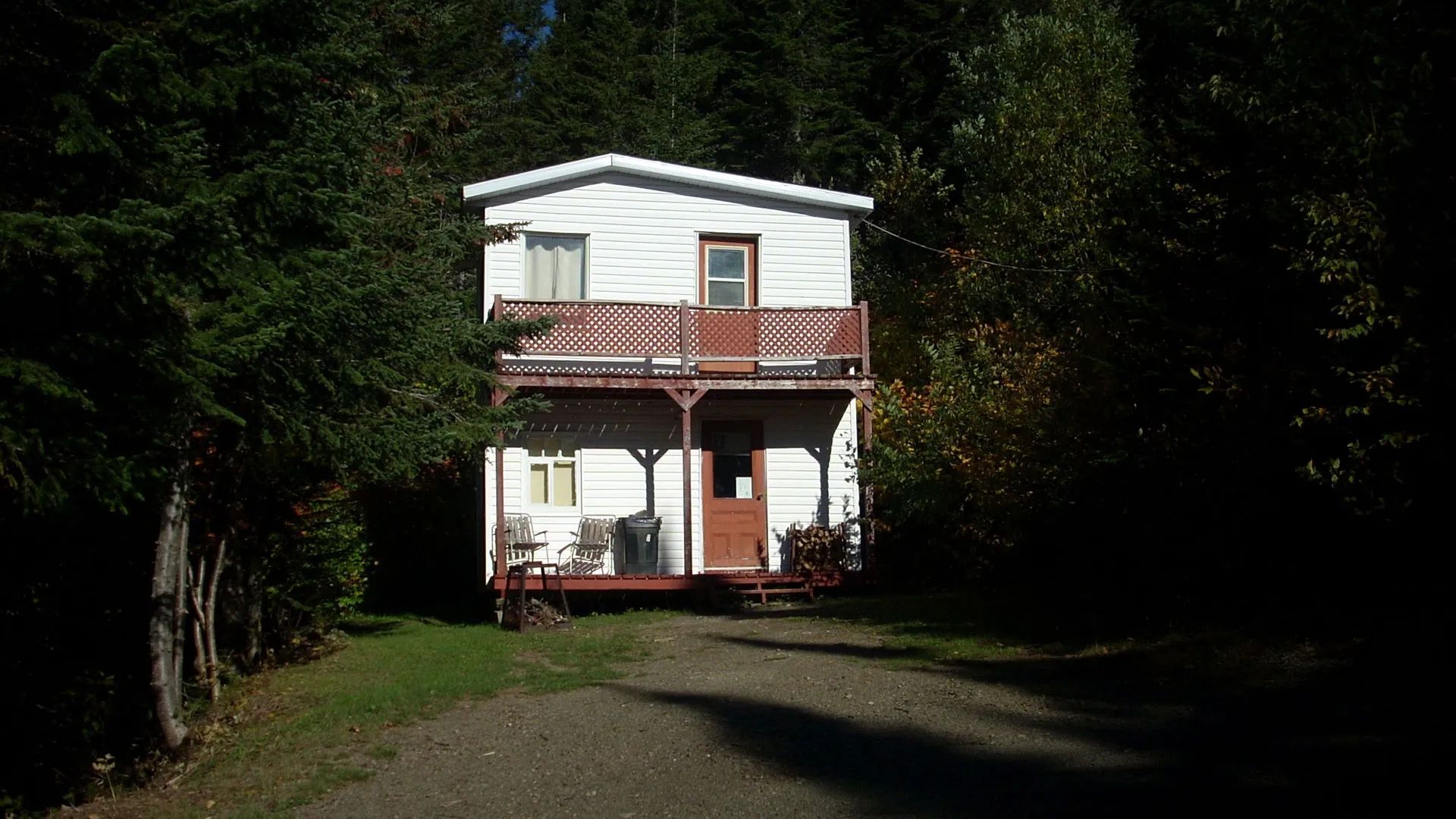 Front view of a two-story cabin surrounded by trees with a balcony and a covered porch.