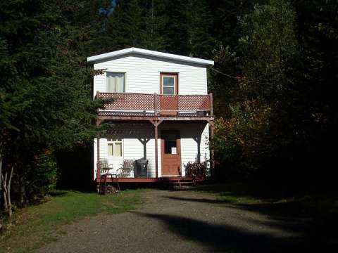 Front view of a two-story cabin surrounded by trees with a balcony and a covered porch.