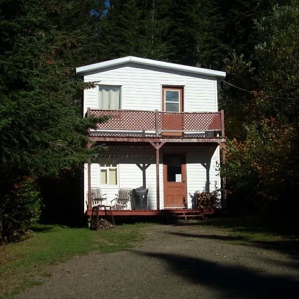 This two-story white wooden cabin features a covered gallery facing the forest.