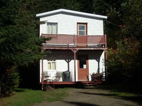 This two-story white wooden cabin features a covered gallery facing the forest.