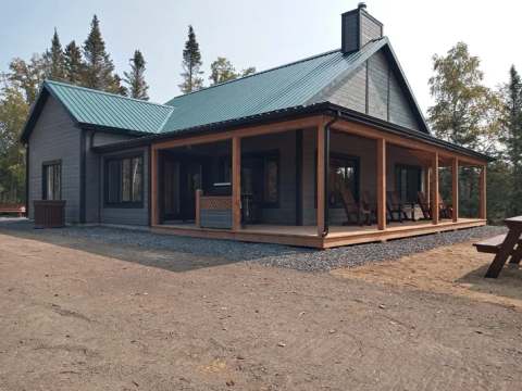 The L'Orignal cabin features a large covered porch with chairs for relaxing in nature.
