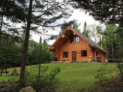 Le chalet en bois rond entouré d'arbres matures offre une galerie avec barbecue.