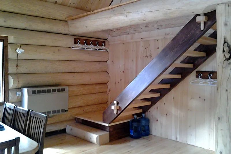 Vue intérieure du chalet Le Pygargue montrant l'escalier en bois et les murs en pièces rondes.