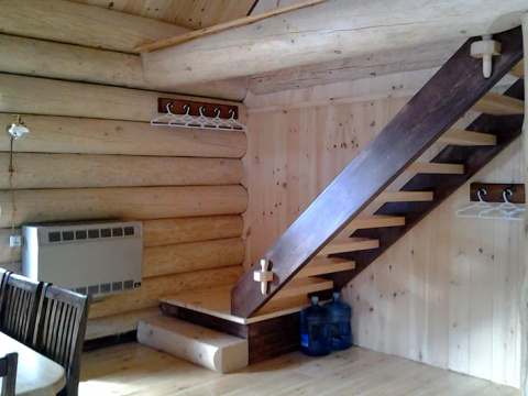 Vue intérieure du chalet Le Pygargue montrant l'escalier en bois et les murs en pièces rondes.