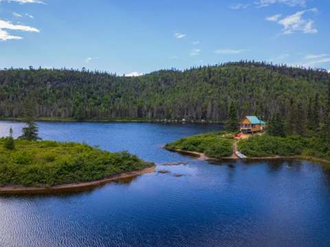 Vue aérienne du chalet isolé au bord du lac entouré de forêt.