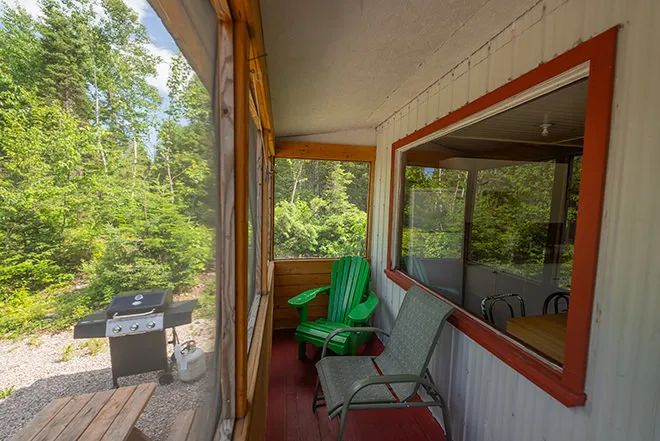 The chalet's screened porch is equipped with chairs for relaxing and an outdoor barbecue.