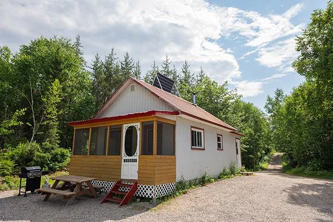 Vue extérieure du chalet avec sa véranda grillagée, sa table de pique-nique et son barbecue.